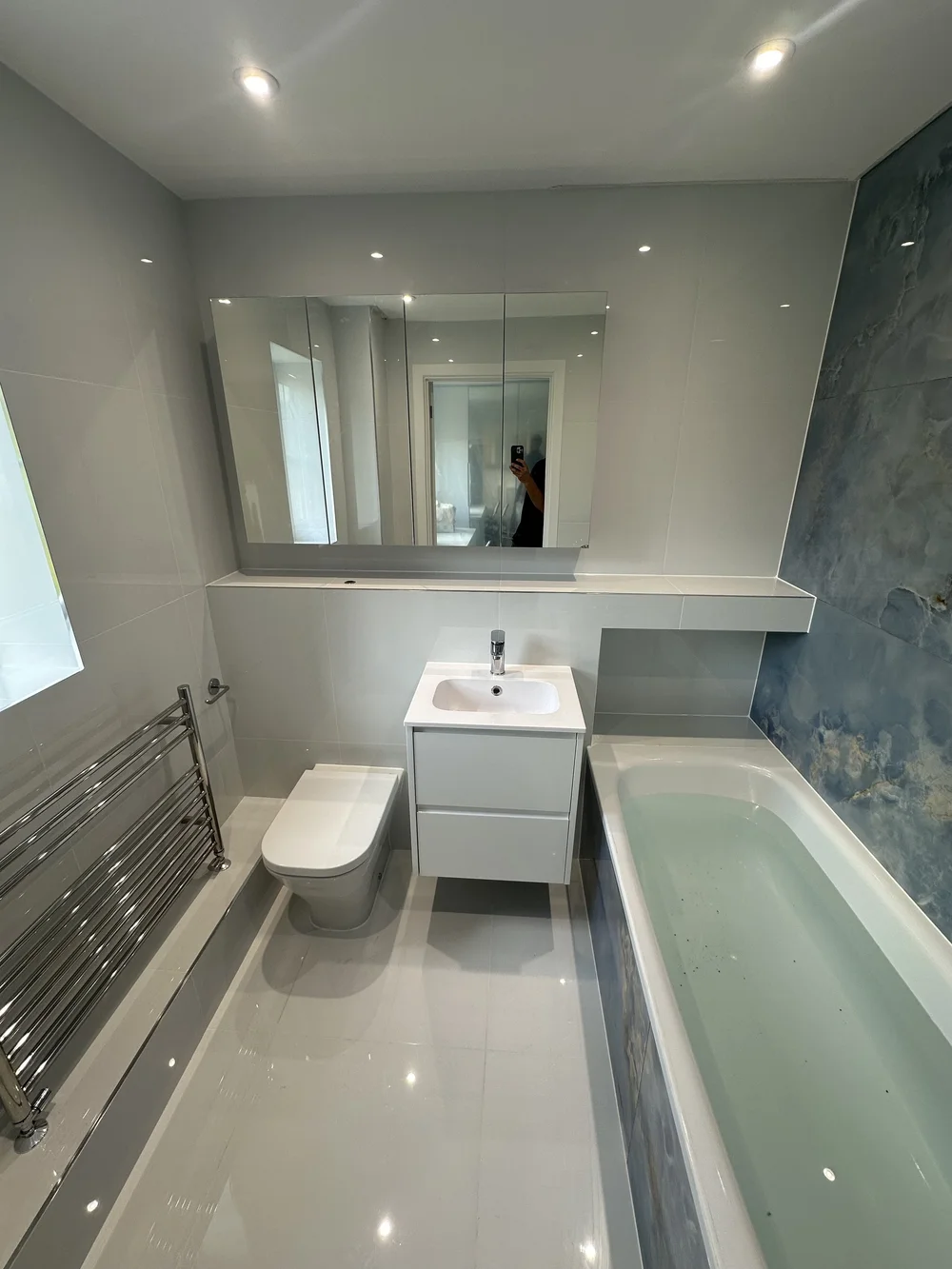 Bright family bathroom with mirrored cabinet, white vanity and blue onyx accent wall — bathroom renovation